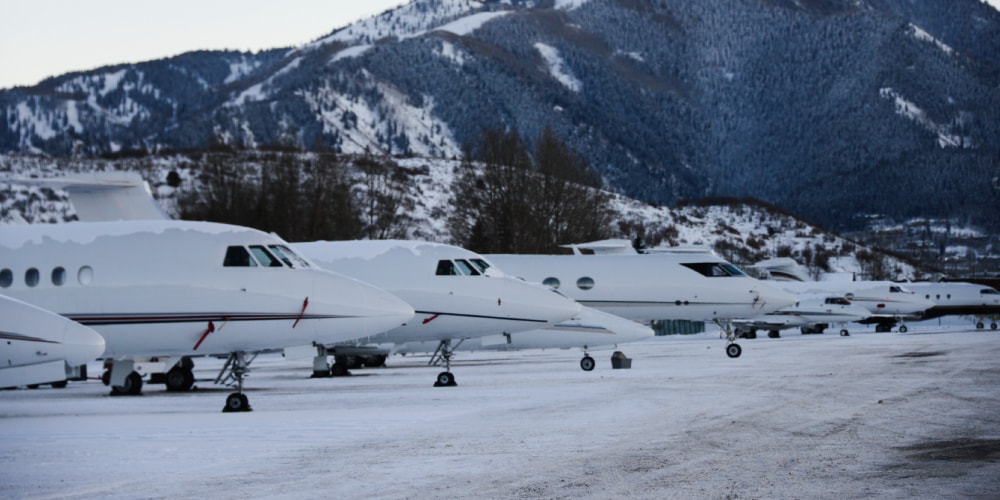 Avions privés alignés dans une zone enneigée avec montagnes en arrière-plan.