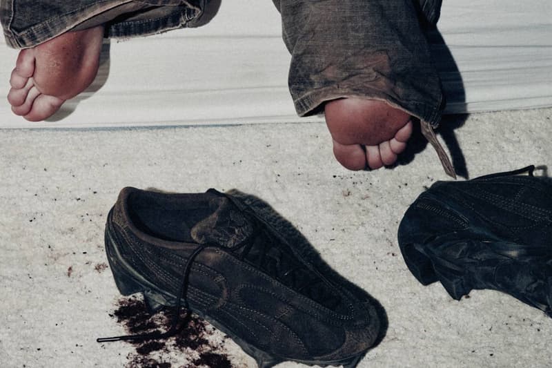 Deux chaussures sales sur le sol près de pieds sur un lit.