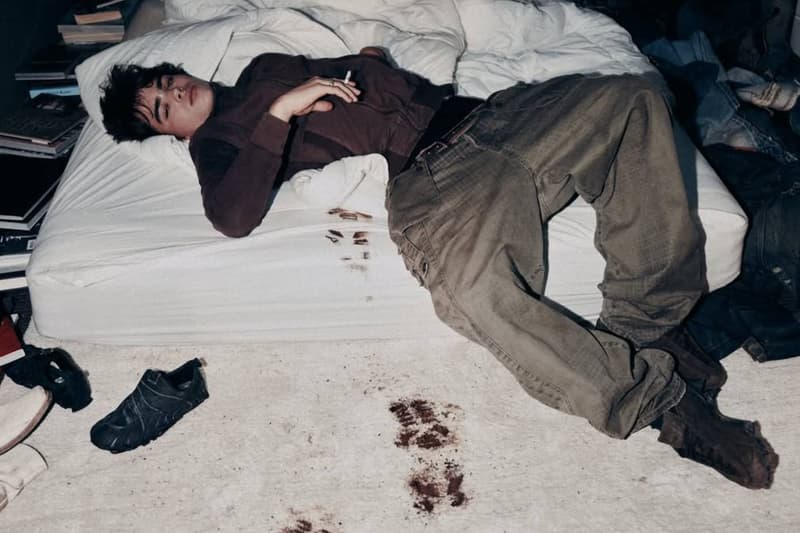Jeune homme allongé sur un lit, traces marron au sol, désordre autour.